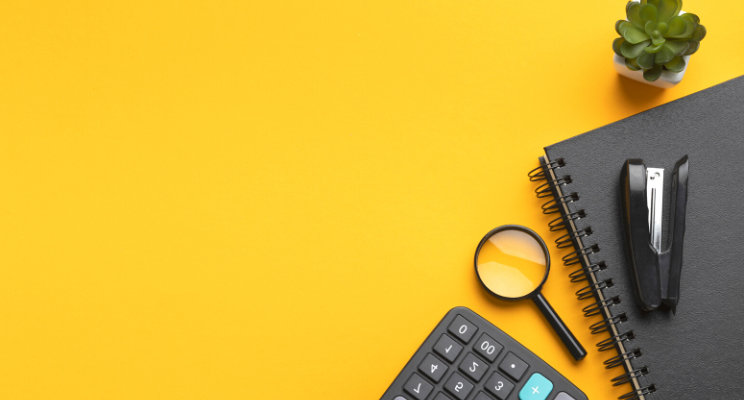 stapler, magnifying glass, calculator, notebook and succulent against a yellow background