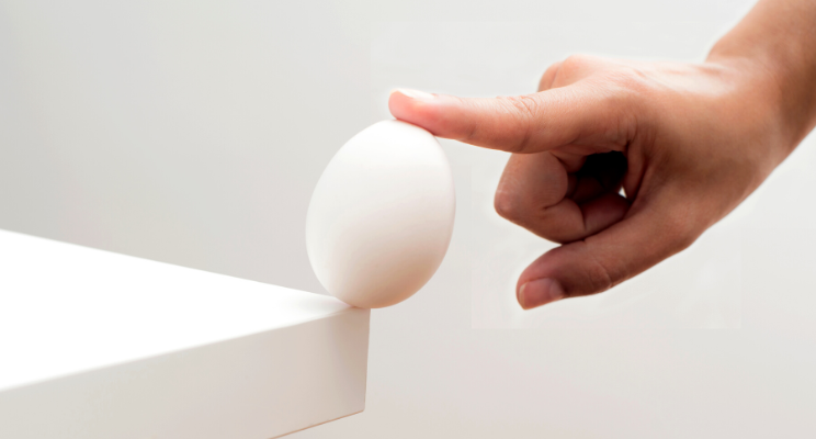a single finger balancing an egg on the edge of a white table